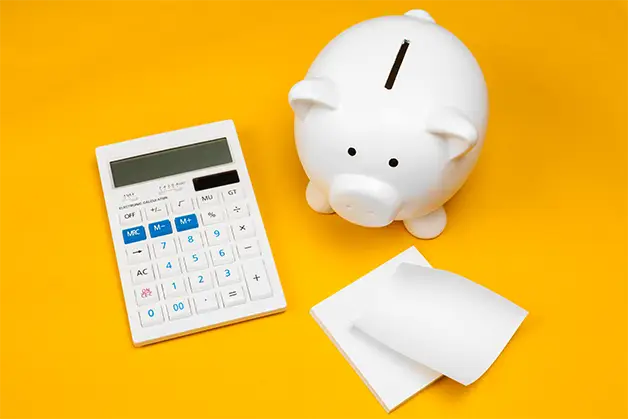 piggybank, calculator, and notepad on a bright yellow table